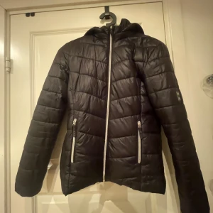 Svart pufferjacka från H&M - Säljer en svart pufferjacka från H&M i storlek 164 som passar perfekt för kyliga dagar. Jackan har en dragkedja framtill och två praktiska fickor med dragkedjor. Den är quiltad och har en huva för extra värme. Perfekt för höst och vinter!