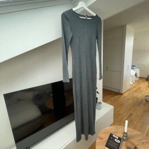 Grå långklänning - Säljer en stilren och enkel grå långklänning. Den är ribbad och har långa ärmar, perfekt för en elegant och avslappnad look. Klänningen är i ett mjukt och bekvämt material, vilket gör den idealisk för både vardag och festligare tillfällen.
