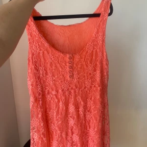 Korallfärgad spetsklänning - Säljer en superfin korallfärgad spetsklänning som är perfekt för sommaren! Den är ärmlös och har en söt knappdetalj framtill. Klänningen är i ett lätt och luftigt material, vilket gör den idealisk för varma dagar. Passar perfekt till både vardag och fest! 🌸