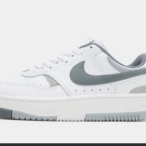 Nike Air Force i vitt och grått - Snygga och stilrena Nike Air Force sneakers i vitt med grå detaljer. Perfekta för vardagsbruk med en klassisk design och bekväm passform. De har en vit sula och grå swoosh-logga på sidan. Oanvända och förpackningen finns med.