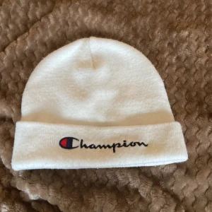 Vit mössa från Champion - Säljer en snygg vit mössa från Champion. Den är supermjuk och har en broderad Champion-logga i blått och rött på framsidan. Perfekt för att hålla sig varm under kalla dagar. Passar de flesta tack vare one size-storleken. 🧢