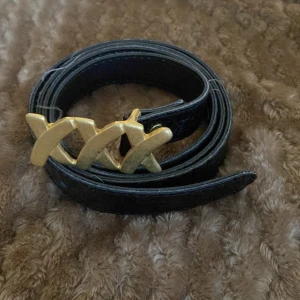 Svart bälte med guldspänne - Säljer ett snyggt svart bälte med ett coolt guldspänne. Bältet har en krokodilskinns-look som ger det en lyxig känsla. Perfekt för att piffa upp vilken outfit som helst! 🖤✨