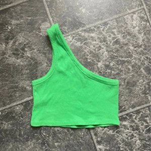 Grön ribbad oneshoulder topp - Säljer en snygg grön ribbad topp med oneshoulder-design. Perfekt för sommardagar eller en utekväll. Toppen är croppad och sitter tight för en stilren look. Storlek XXS men passar XS, samt passar storlek S men det är med en tajtare passform