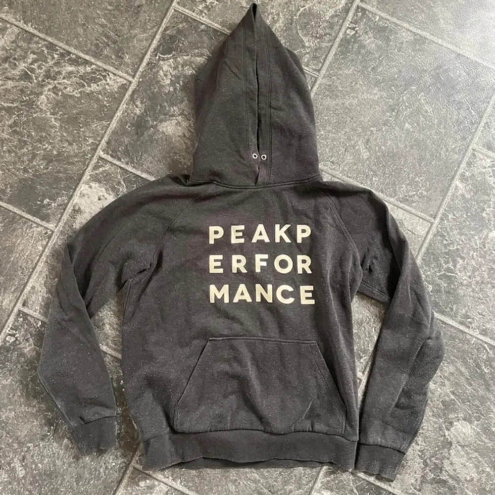 Säljer en mörkgrå hoodie från Peak Performance. Den är supermjuk och perfekt för kyliga dagar. Hoodien har en stor ficka fram och texten 'PEAK PERFORMANCE' i vitt på bröstet. Den är långärmad och har en klassisk passform. Perfekt för både vardag och chill! Storlek M men passar superbra till S också. Lite nopprig som är enkelt att få bort, annars inga defekter.. Tröjor & Koftor.