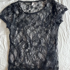 Svart spetsblus - Säljer en svart spetsblus med korta ärmar. Blusen är genomskinlig och har ett vackert mönster i spetsen.