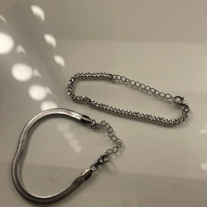Två silverarmband - Säljer två stilrena silverarmband. Det ena har en ormliknande design med en slät yta, medan det andra har en klassisk kedjedesign