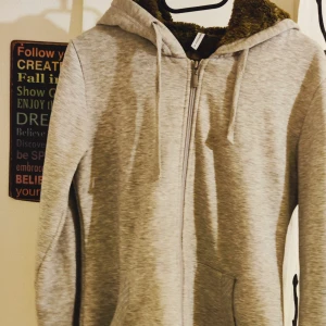 Grå hoodie med fuskpälsfoder - Säljer en supermysig grå hoodie från GAP. Den har ett mjukt fuskpälsfoder i luvan som gör den perfekt för kyliga dagar. Dragkedja framtill och praktiska fickor. Perfekt för både höst och vinter!