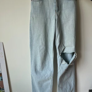 Ljusa jeans från Zara - Säljer ett par ljusa jeans från Zara i storlek S. De har en avslappnad passform med en stor reva på ena benet för en trendig look. Perfekta för en casual stil!