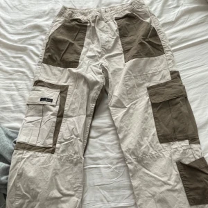 Beige och bruna cargopants - Säljer ett par snygga cargopants i beige och brunt. De har flera praktiska fickor och en loose passform. Perfekta för en avslappnad stil eller utomhusaktiviteter. Använda 1 gång 