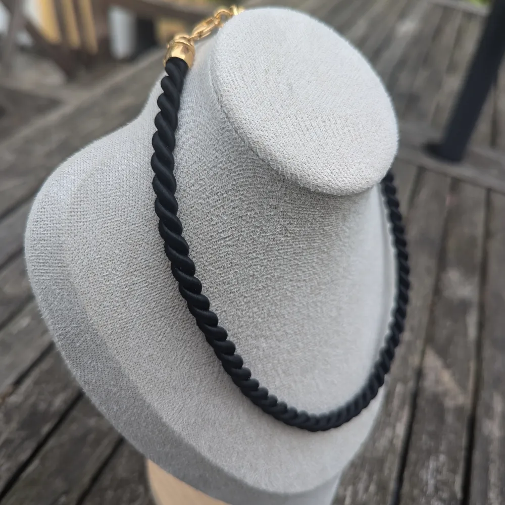 Svart halsband med en tvinnad design. Halsbandet har snygga gulddetaljer vid låset.mycket fint skick. Accessoarer.