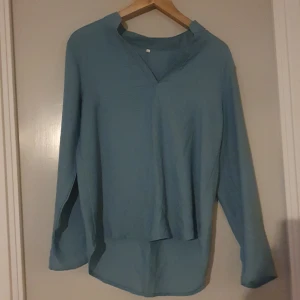 Blå långärmad tröja - Säljer en stilren långärmad turkosblus i storlek XL Perfekt för både vardag och lite finare tillfällen. Tröjan har en enkel design med en v-ringad hals.