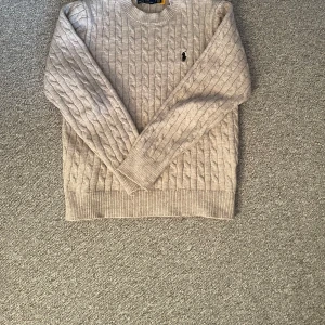 Grå stickad tröja från Ralph Lauren - Säljer en stilren beige stickad tröja från Ralph Lauren. Tröjan har ett klassiskt flätmönster och långa ärmar. Perfekt för kyligare dagar och ger en tidlös look. 🧶Storlek S men passar som XS.    Obs: inte säker på om den är äkta 