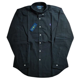 Svart Ralph Lauren-skjorta – Helt ny!! - Stilren och tidlös svart skjorta från Ralph Lauren i slim fit. Tillverkad i ett stretchigt material för extra komfort. Skjortan har långa ärmar, knäppning framtill och pryds av den klassiska broderade loggan på bröstet. 🔥