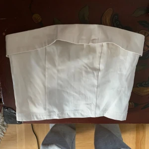 Vit axelbandslös tubtopp - Snygg vit axelbandslös tubtopp i ett stilrent och enkelt utförande. Perfekt för varma dagar eller som basplagg under en kavaj. Toppen har en ren design utan extra detaljer.