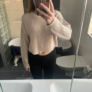 Beige stickad croppad tröja - Säljer en snygg beige stickad tröja med croppad passform. Tröjan har långa ärmar och en rund halsringning.