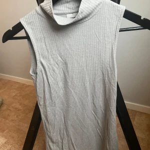 Grå ribbad ärmlös polotopp från Noisy May - Säljer en stilren grå ribbad polotopp från Noisy May. Toppen är ärmlös och har en hög krage som ger en modern look. Perfekt för lager-på-lager eller att bära som den är.