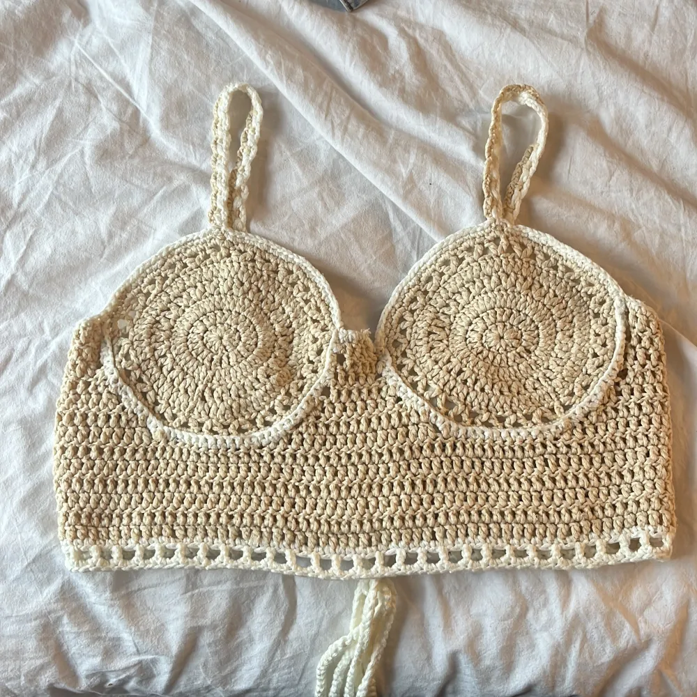 Säljer en snygg beige virkad topp med smala axelband och snörning i ryggen. Toppen har en unik design med cirkulära mönster framtill och är perfekt för sommardagar. Då den har ett inner tyg vid brösten kan den användas utan bh💕Den är croppad och ger en bohemisk vibe💕 knappt använd därför i väldigt bra skick! Passar xs-s.. Yläosat.