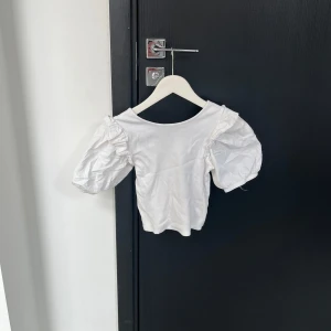 Vit blus med puffärmar - Säljer en söt vit blus med puffiga kortärmar och volangdetaljer. Perfekt för en stilren och romantisk look. Blusen har en rund halsringning och är gjord i ett lätt material.