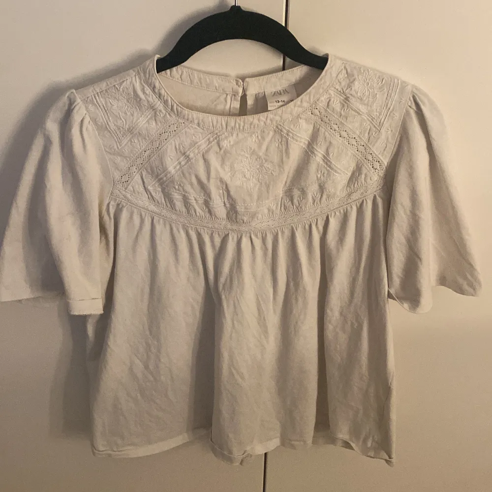 Charmig vit blus med spetsdetaljer på bröstet och trekvartsärmar. Perfekt för en stilren och elegant look. Blusen har en luftig passform och knäppning i nacken.. Yläosat.