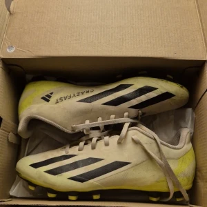 Adidas X Crazyfast.4 Fotbollsskor - Säljer ett par Adidas X Crazyfast.4 fotbollsskor i vit och grön färg med svarta detaljer. Skorna har snörning och är designade för fotboll. Perfekta för snabba rörelser på planen.