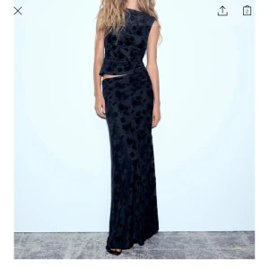 Søger dette set🩷 - Elegant svart långklänning med ett subtilt blommigt mönster. Klänningen har en ärmlös design och en figurnära passform som framhäver silhuetten. Perfekt för en stilfull kväll.