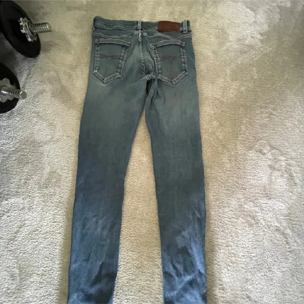 Snygga blå jeans med en klassisk femficksdesign och en läderdetalj vid midjan. De har en smal passform och är perfekta för en avslappnad stil. Jeansen har en lätt tvättad look som ger dem en cool vibe.. Farkut & Housut.
