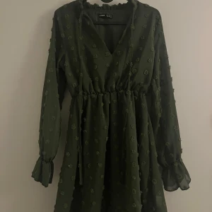 Mörkgrön klänning med knyt - Snygg mörkgrön klänning från Shein med v-ringning och knytband framtill. Klänningen har långa ärmar och ett diskret prickigt mönster. Perfekt för en stilren look.