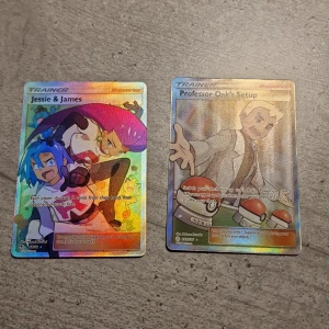 Pokémon Trainer-kort: Jessie & James och Professor Oak's Setup - Säljer två holografiska Pokémon Trainer-kort: Jessie & James och Professor Oak's Setup. Jessie & James-kortet har en färgglad design med karaktärerna i fokus, medan Professor Oak's Setup visar Professor Oak med Pokébollar. Perfekt för samlare eller spelare som vill förstärka sin kortlek.