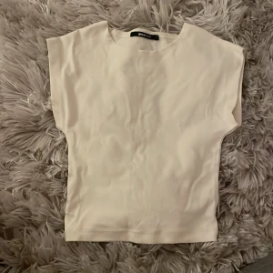 Vit topp från Gina Tricot - Säljer en jättegullig vit/gul topp från Gina Tricot i storlek S. Toppen har en enkel design med korta ärmar och är även ganska kort. Perfekt för en minimalistisk look.