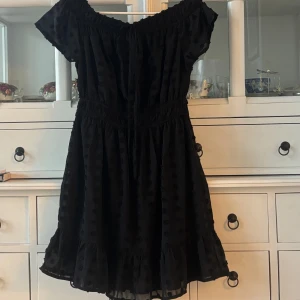 Svart klänning från Charlotte Russe - Svart klänning från Charlotte Russe i New York med prickigt mönster och offshoulder-design. Klänningen har volangdetaljer vid fållen och en elastisk midja för en bekväm passform. Perfekt för en stilren look.