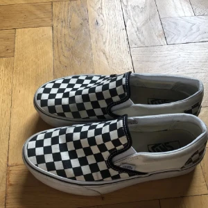 Svartvita slip-on sneakers från Vans - Klassiska sneakers från Vans med ett ikoniskt rutigt mönster. Dem e såååå fina men tyvärr för små och är lite smutsiga men d kan man lätt ta bort