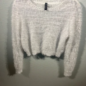Vit fluffig tröja från H&M Divided - Mysig vit fluffig tröja från H&M Divided. Perfekt för kyliga dagar med sin mjuka och varma känsla. Tröjan har en croppad design och långa ärmar, vilket ger en trendig look. Ett måste i garderoben för en stilren och bekväm outfit.