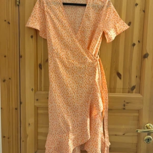 Rosa leopardmönstrad omlottklänning - Säljer en söt orange omlottklänning med leopardmönster. Klänningen har korta ärmar och en v-ringad design som ger en feminin touch. Perfekt för sommarens varma dagar! 🧡