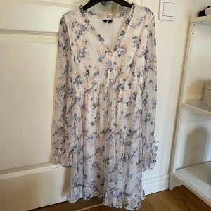 Blommig klänning från Vero Moda - Säljer en söt blommig klänning från Vero Moda i ljusa toner. Klänningen har långa ärmar med volangdetaljer vid ärmslut och en v-ringad hals. Perfekt för skolavslutningen.