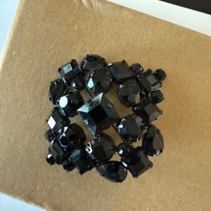 Svart glittrig brosch  - Snygg svart brosch med glittriga stenar i olika former och storlekar. Perfekt för att ge en elegant touch till din outfit. 
