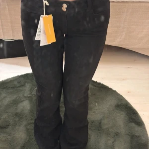 Svarta jeans med bootcut - Snygga svarta jeans med bootcut och låg midja. De har en design med knappar där bak. Barn storlek helt nya