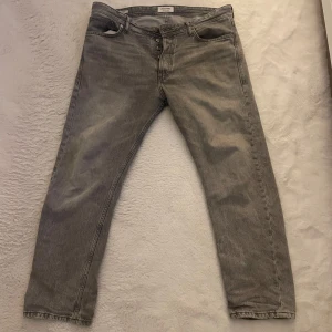 Grå jeansbyxor Jack and Jones - Snygga grå jeansbyxor med en klassisk femficksdesign och knappgylf. Perfekta för en avslappnad stil med en rak passform som ger en tidlös look.