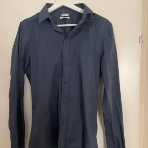 Mörkblå skjorta från Filippa K - Snygg mörkblå skjorta från Filippa K i storlek S. Skjortan har en klassisk krage och knappar framtill. Perfekt för en stilren look.