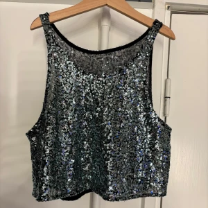 Glittrig paljettopp - Snygg glittrig paljettopp i silver med ärmlös design. Perfekt för en festlig kväll. Toppen har en croppad passform och är täckt av glittrande paljetter som fångar ljuset.