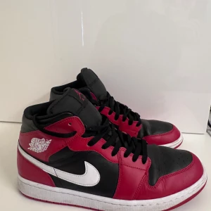 Nike Air Jordans i svart och röd - Snygga Nike Air Jordans i en klassisk svart och röd färgkombination med vit sula och logotyp. Skorna har snörning och en hög design som ger extra stöd och stil. Perfekta för dig som vill ha en ikonisk look.