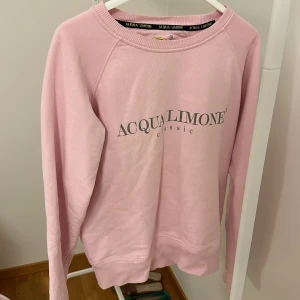 Rosa sweatshirt från Acqua Limone - Säljer en rosa sweatshirt från Acqua Limone med tryck fram och ett stort gult citronmotiv på baksidan. Tröjan har långa ärmar och rund halsringning. Perfekt för en avslappnad stil.