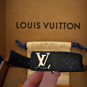 LV Slim Bracelet - Elegant Louis Vuitton armband i Monogram Eclipse canvas. Armbandet har en stilren design med LV-logotypen i silver på framsidan. Fint skick, första hålet (största) är lite slitet men fungerar fortfarande, köpt för 3200 på deras hemsida.
