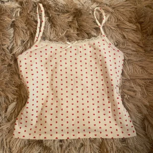 vitt linne med hjärtan från Gina Tricot - Söt vitt linne från Gina Tricot med röda hjärtan och spetsdetaljer. Axelbanden är smala och justerbara. endast provad, som nytt skick. 