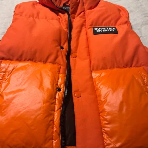 Orange dunjacka från Duvetica - Säljer en snygg orange dunjacka från Duvetica. Jackan har en dragkedja och knappar framtill samt stora fickor. Perfekt för att hålla värmen under kyligare dagar under våren och hösten. Skicket är 10/10! 