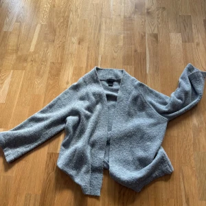 Grå kofta från Lindex - Mysig grå kofta från Lindex i en mjuk och fluffig textur. Perfekt för kyliga dagar med sin avslappnade passform och trekvartsärmad. Enkel att matcha med olika outfits.