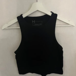 Svart ribbad linnetopp från Essentiel Antwerp - Snygg svart ribbad linnetopp från Essentiel Antwerp. Perfekt för en stilren look med sin ärmlösa design och croppade passform. Ett mångsidigt plagg för din garderob.