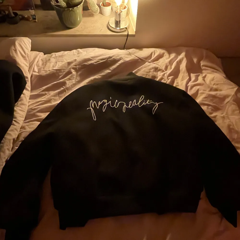Snygg svart bomberjacka med knappar och broderad text på ryggen. Perfekt för en cool och avslappnad stil.. Takit.