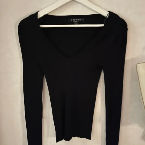 Svart v-ringad tröja från Amisu - Snygg svart v-ringad tröja från Amisu i stickat material. Perfekt för en stilren look med långa ärmar och en figurnära passform. Enkelt att matcha med olika outfits.