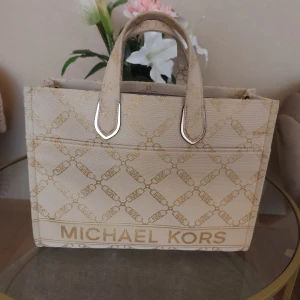 Beige shoppingväska från Michael Kors - Snygg beige shoppingväska från Michael Kors med logotypmönster och två handtag. Perfekt för en dag på stan eller som en stilren accessoar. Väskan har en rymlig design och är lätt att matcha med olika outfits. Nypris var 4500 