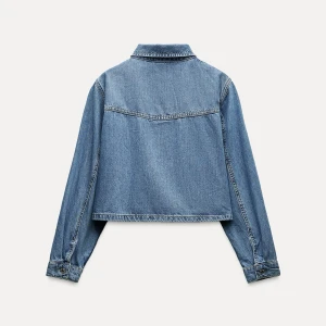 Blå croppad jeansjacka från Zara - Säljer en snygg blå croppad jeansjacka från Zara. Jackan har en klassisk krage, knappar framtill och en bröstficka. Perfekt för en avslappnad stil.
